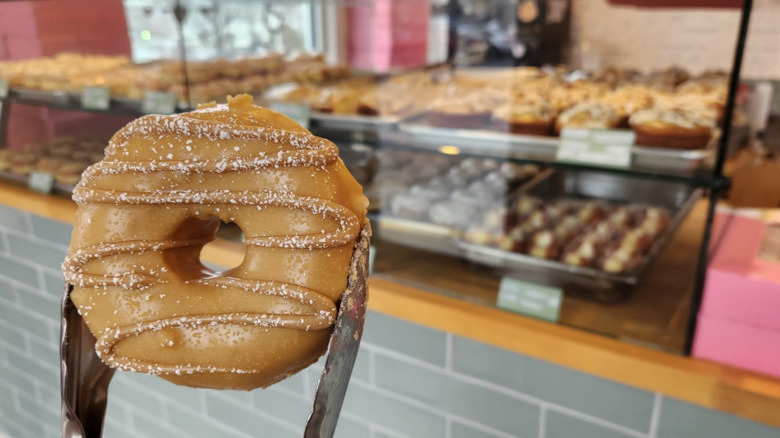 Pair of tongs holding a donut in front of bakery case