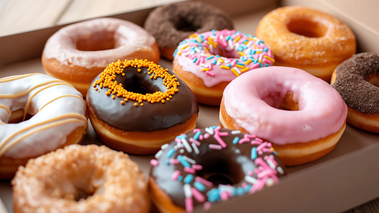 Glazed and decorated donuts in a box, showcasing a variety of flavors and toppings, with vibrant icing colors, set on a wooden tabl