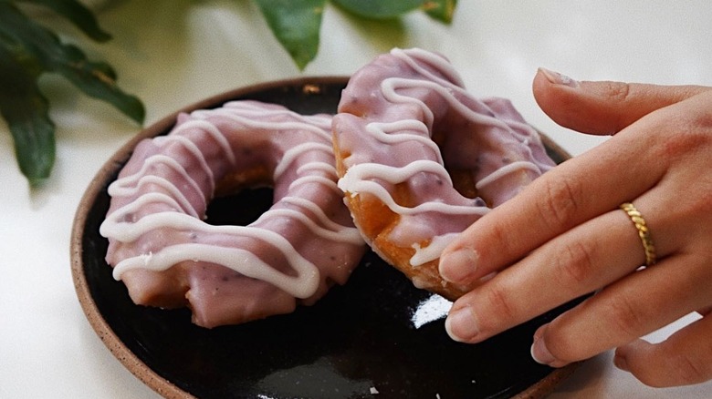 Hand reaching for two blueberry old fashioned donuts on a plate