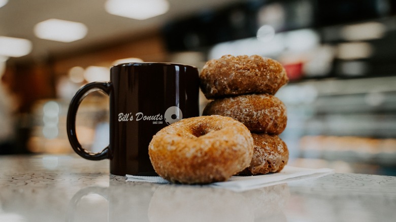 Stack of fresh donuts next to a mug of coffee on a counter