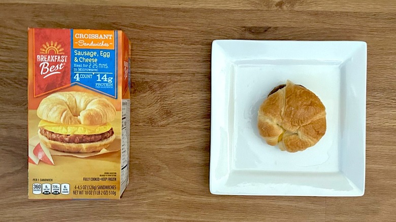 Package and cooked Breakfast Best Croissant Sandwiches Sausage, Egg, & Cheese on square white plate