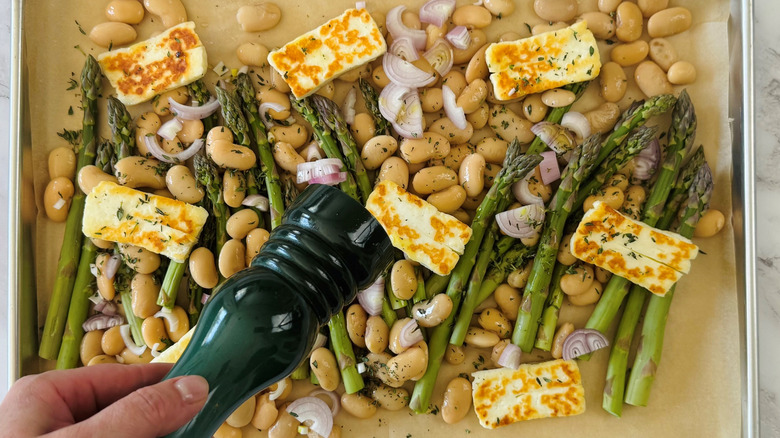 hand holding pepper grinder over sheet pan