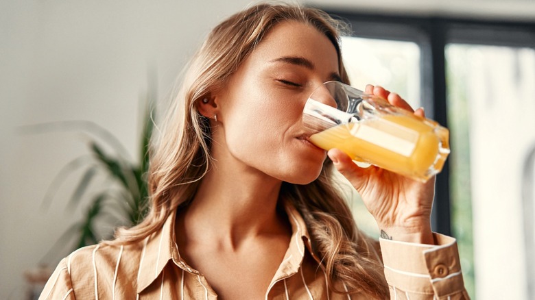 blonde woman drinks orange juice from glass