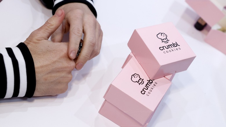 crumbl cookie boxes on tabletop with folded hands