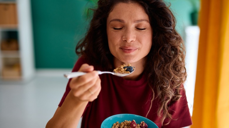 woman eats a bowl of breakfast cereal with fruit