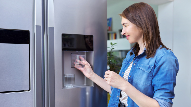 Woman fills two glasses of water at a fridge water dispenser