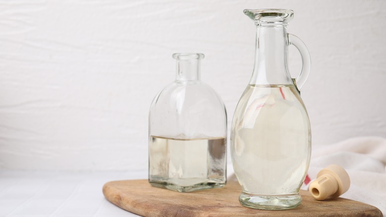 Two glass bottles of white vinegar on wooden cutting board
