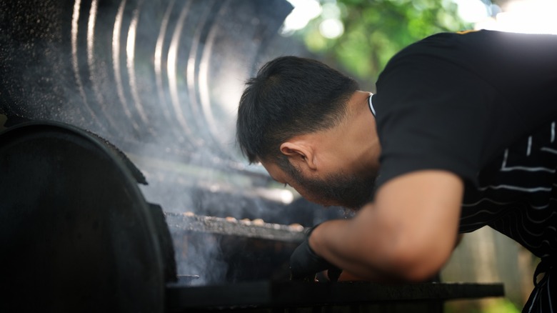 man leans into cooking smoker