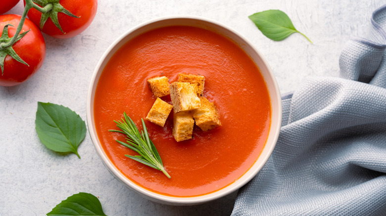 A top-down view of tomato soup with croutons and rosemary