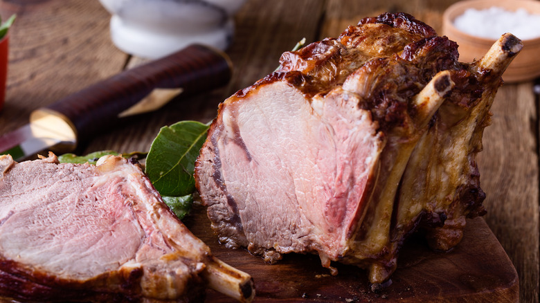 A cooked, bone-in rib roast being sliced, on a wooden table