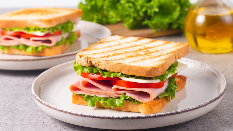 A close-up of two club sandwiches, one in the foreground and one in the background, with a jug of olive oil and some kale also in the background
