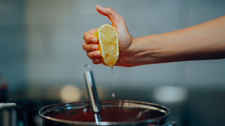 Hand squeezing half a lemon into a pot of soup on the stove