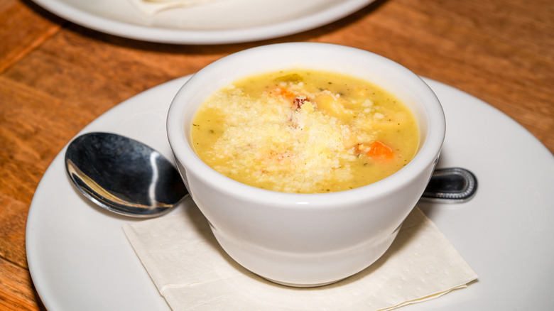 A cup of yellow chicken noodle soup with finely grated parmesan cheese on top