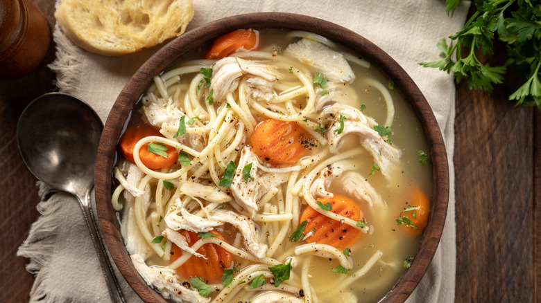 Wooden bowl of chicken noodle soup with long noodles and carrots