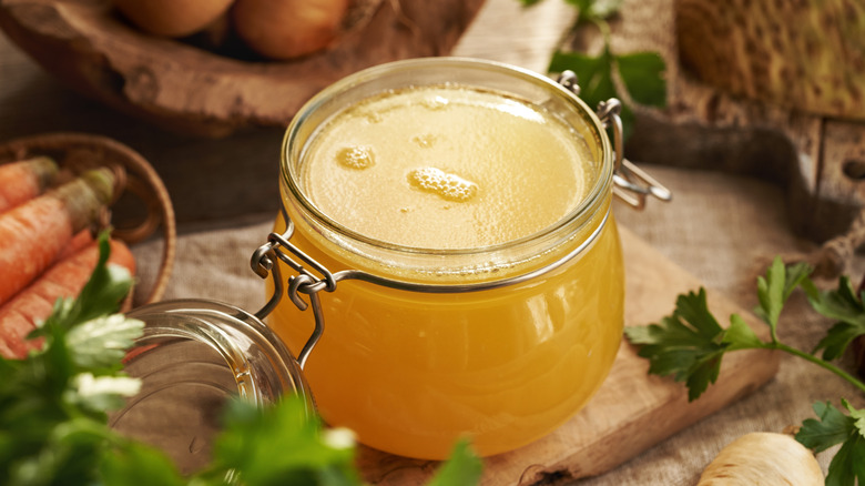 A jar of chicken bone broth with onions, parsley and carrots