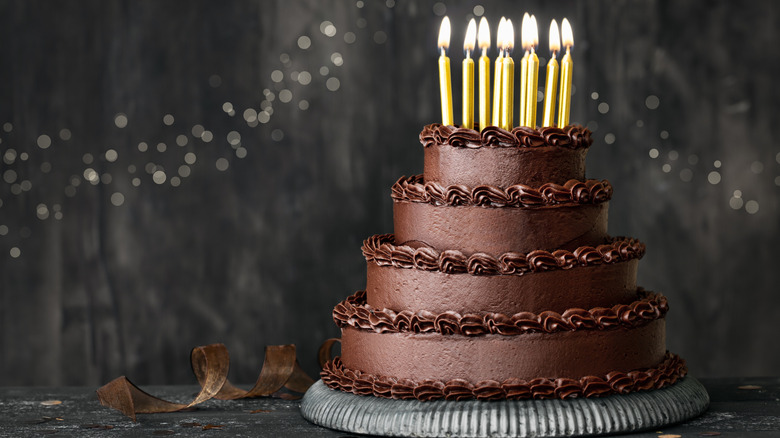 Tiered chocolate birthday cake with lit candles.