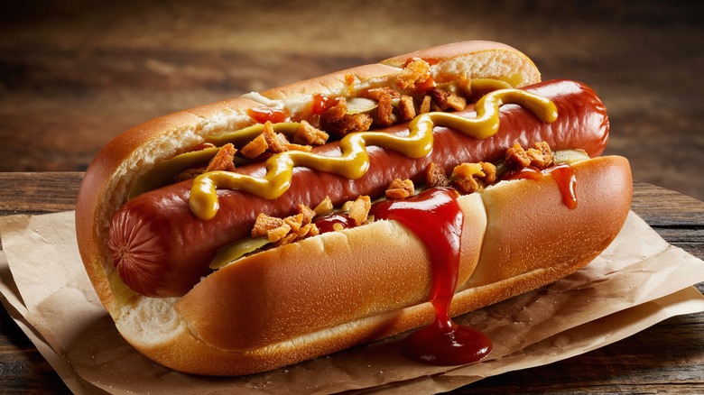 A close-up of someone squeezing ketchup onto a hot dog with a bun