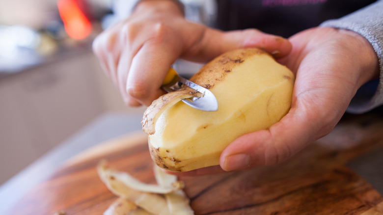 Someone peeling a potato with a peeler