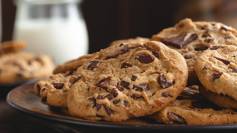 Closeup of chocolate chip cookies on a plate with glass of milk in background