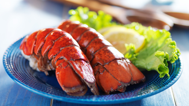 A close-up of two cooked lobster tails on a blue plate with lettuce and lemon slices