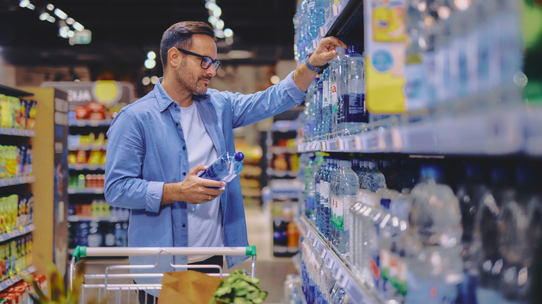 Man looks at variety of bottle water brands on grocery shelves.