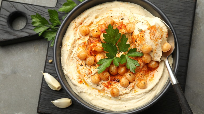 Bowl of hummus with chickpeas, paprika, and parsley on top with spoon