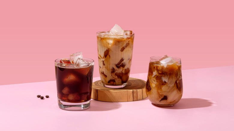 Three glasses of iced coffee on pink surface and pink background.
