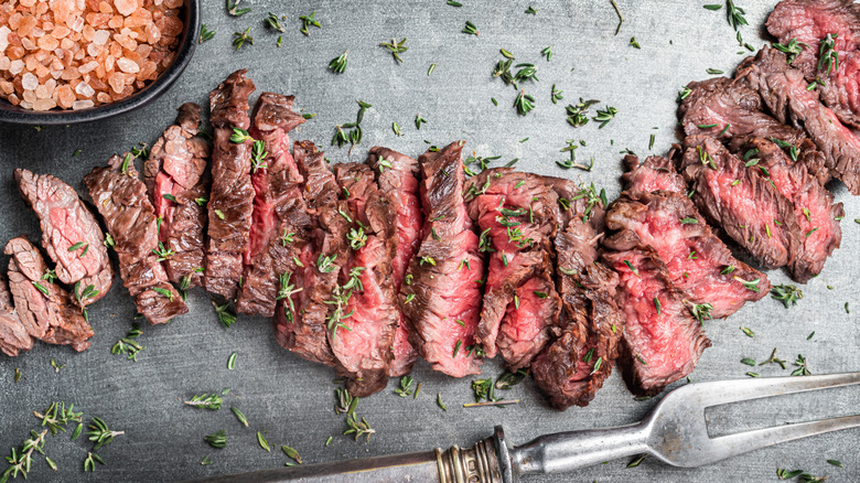 Sliced skirt steak on a steel tray with thyme