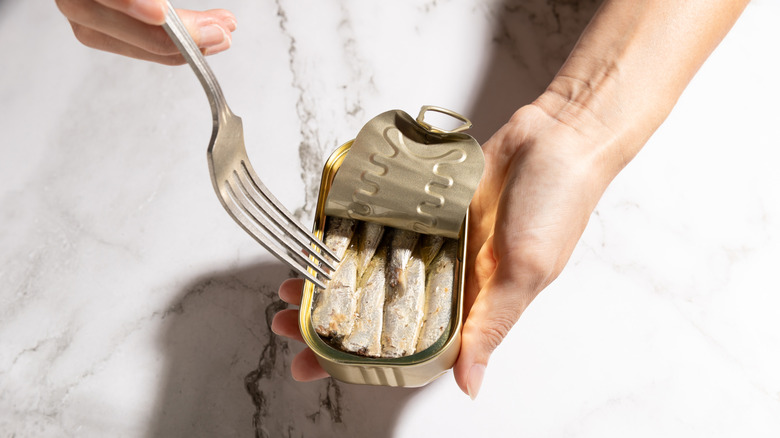 Hands using fork to get sardines from tin.