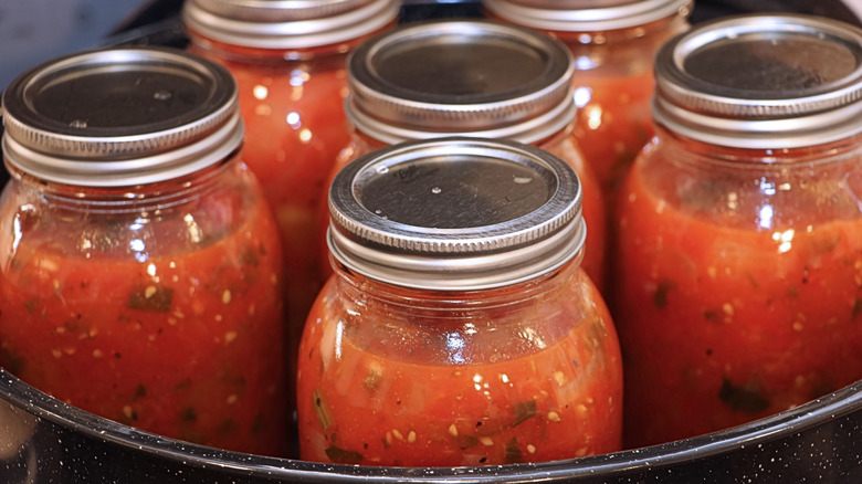 Closeup of canning jars with tomatoes inside, in water bath.
