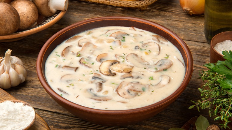 Cream of mushroom soup in a terracotta bowl surrounded by its ingredients.