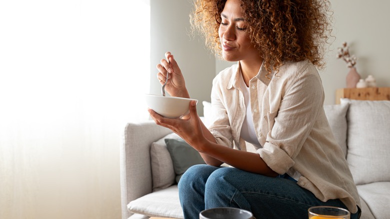 woman eats bowl of cereal on couch