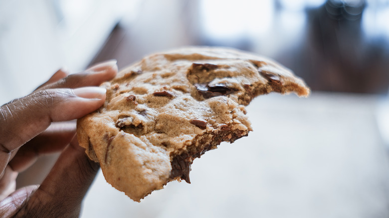 Closeup of hand holding a chocolate chip cookie with bites taken out of it