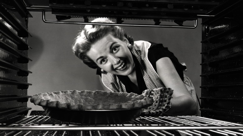 old-school home baker peeks at a pie in the oven
