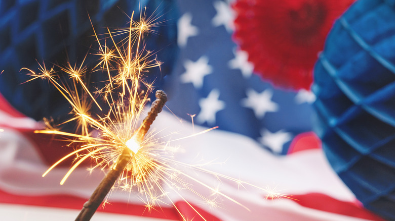 lit sparkler in front of patriotic decorations for 4th of july