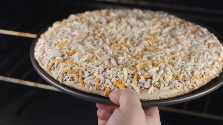 Person putting frozen cheese pizza in oven