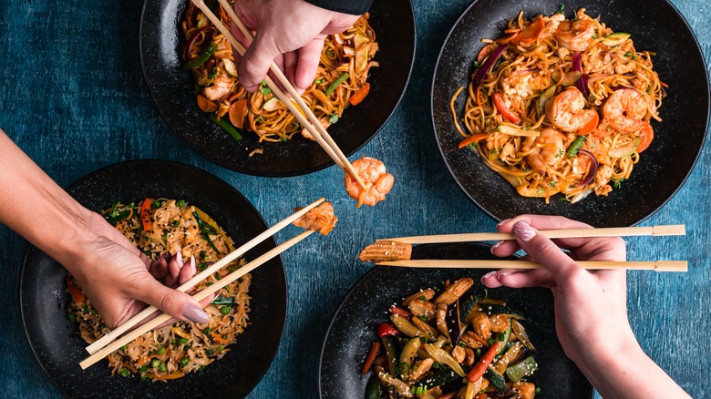 Hand holding chopsticks over multiple dishes