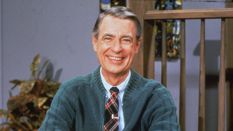 Mister Rogers smiling for the camera in his trademark sweater and tie