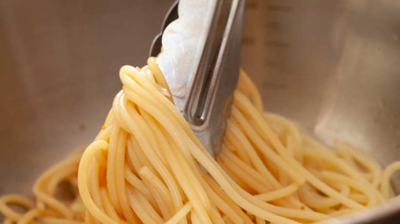Close-up of metal tongs holding cooked spaghetti