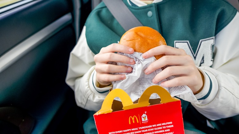 young person eats hamburger from happy meal box