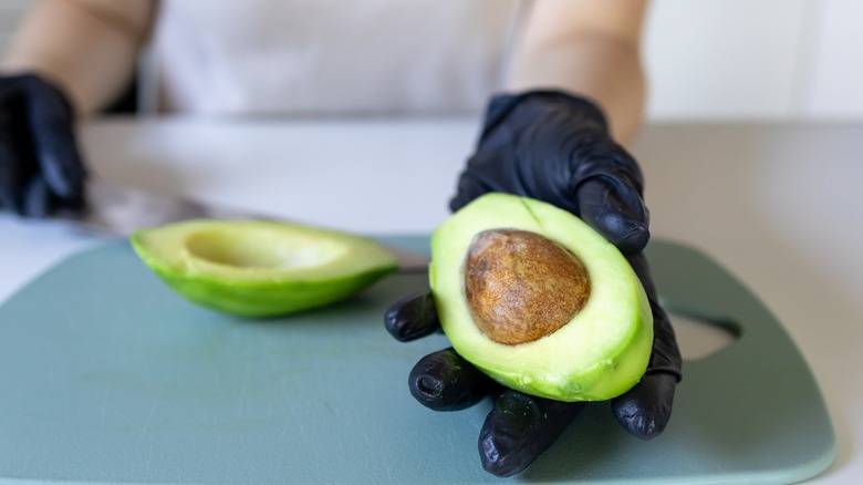 gloved hands hold split avocado