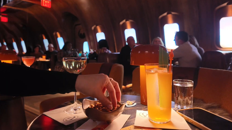 Handing reaching into bowl of bar snacks on table with cocktails.
