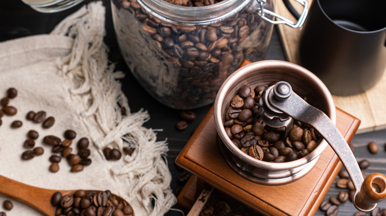 Whole coffee beans in jar and hand grinder next to it.