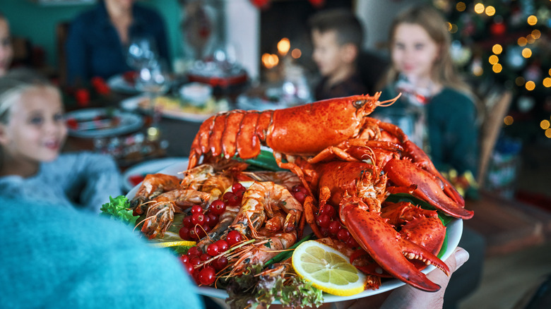 A close-up of a dish of lobster and other seafood on a plate at a festive holiday dinner, with blurry kids sitting at the table in the background