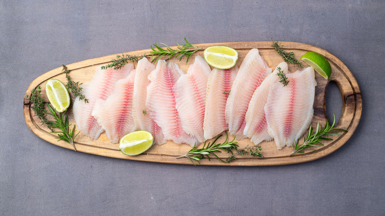 tilapia filets with citrus and herbs on oval cutting board