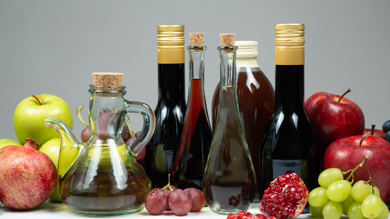 Bottles of different types of vinegar in a row, surrounded by fruits