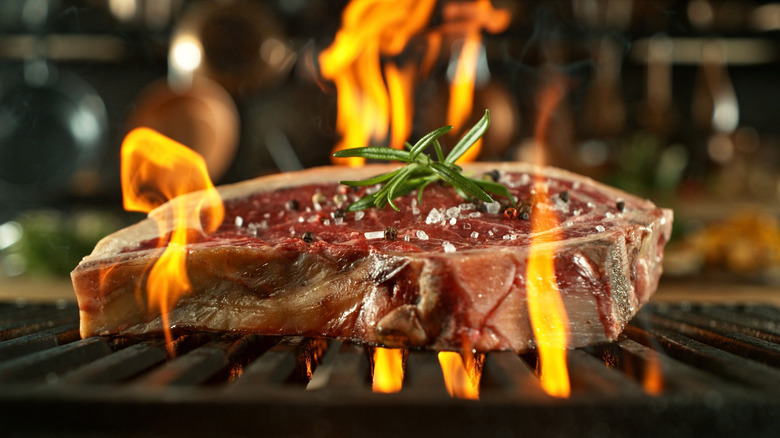 Steak on a grill, sprinkled with salt and pepper and garnished with herb, with fire coming from below