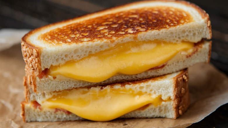 A gooey grilled cheese sandwich cut in half oozing cheese on top of a rustic tree stump