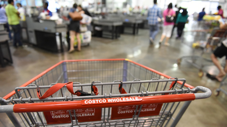 Closeup of costco shopping cart with customers in background.