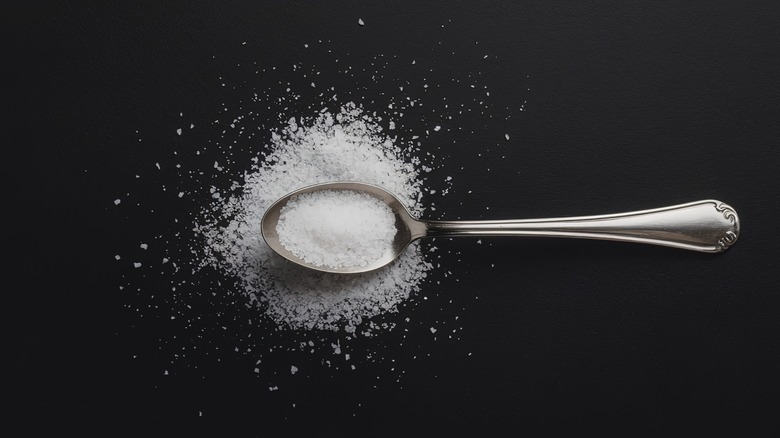silver teaspoon with salt on black background